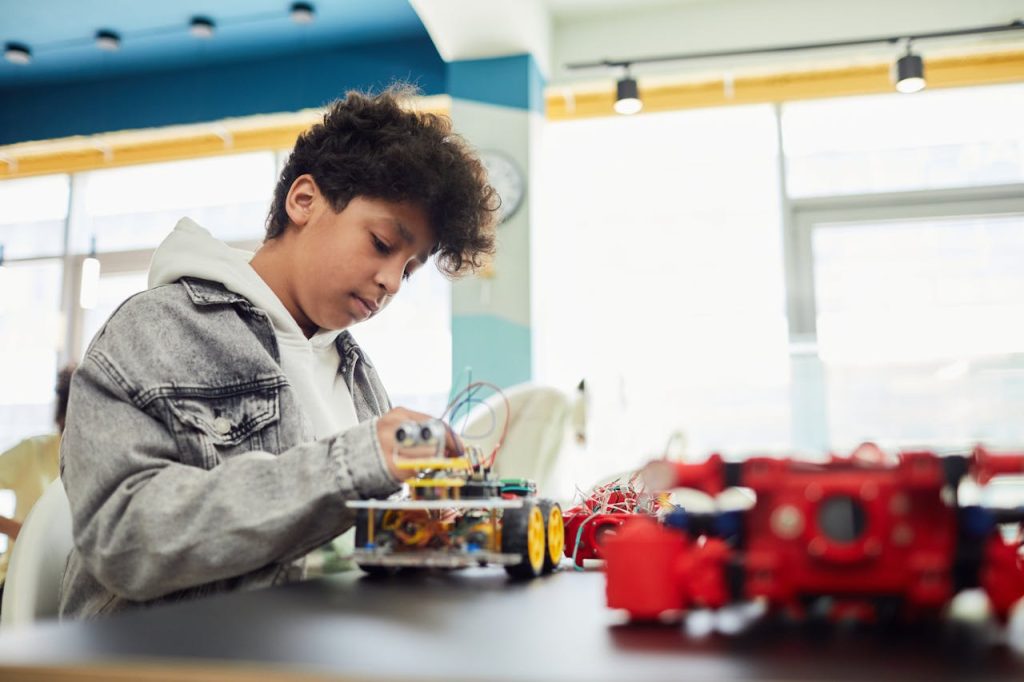 A young student focused on building a robotic toy car in a modern indoor setting.